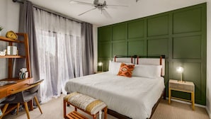 A bedroom with a bed, a desk, a chair, a bench, a bedside table, and a ceiling fan.