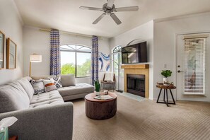 A living room with a sofa, a coffee table, a fireplace, a television, and a door with blinds.