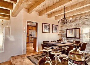 A dining area with a long table, chairs, and a chandelier. There are framed pictures on the wall and a large mirror. - Desert Retreat House with Pool and Casita 15 minutes from Downtown  (Santa Fe)