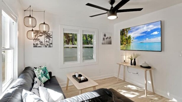A modern living room with a sofa, coffee table, and a TV mounted on the wall. - ModernTropic 2bd/1ba Near Beach w/ fence yard/deck (Lake Worth)