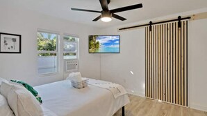 A bedroom with a bed, a ceiling fan, a TV, and a sliding door. - ModernTropic 2bd/1ba Near Beach w/ fence yard/deck (Lake Worth)