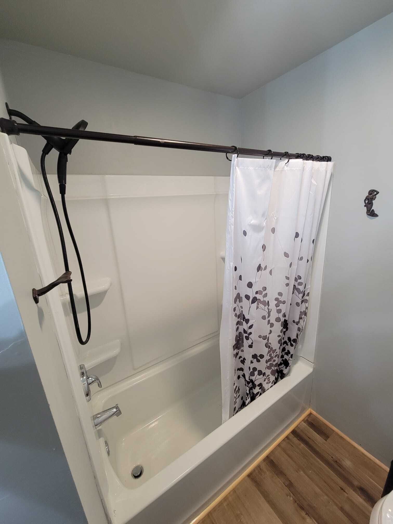 A shower with a black hose and a white shower curtain with a floral pattern.