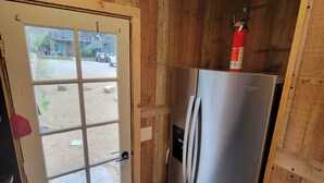 Uma cozinha compacta com geladeira de aço inoxidável, porta de madeira com painel de vidro e extintor de incêndio fixado na parede.