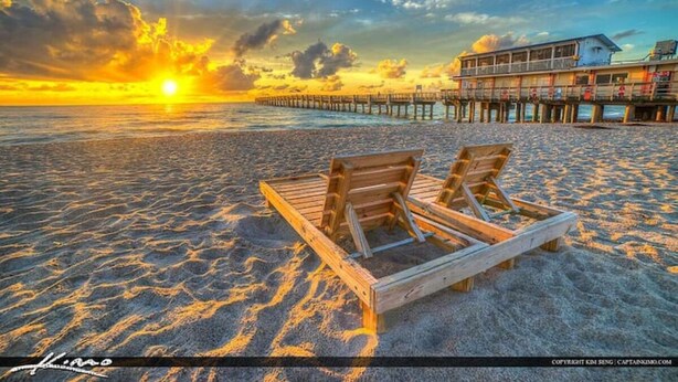 A beach with wooden lounge chairs and a pier in the background.