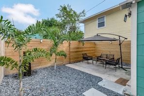 Un jardin avec une clôture en bois, une terrasse avec une table et des chaises, et un petit arbre.