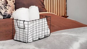 A bedroom with a striped wooden headboard, a bed with brown bedding, a white pillow, and a metal basket on the floor.