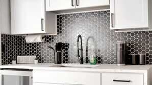 A modern kitchen with white cabinets, a hexagonal tile backsplash, a stainless steel sink, and a coffee maker.