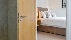 A bedroom with a wooden door, a bed with white bedding, and a nightstand with a lamp. - Canadian timber lodge with direct views to the Alpacas. (Rowrah, near Cockermouth)