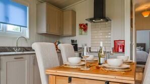 A modern kitchen with white cabinetry, a dining table set with white plates and wine glasses, and a red bag on the counter. - Canadian timber lodge with direct views to the Alpacas. (Rowrah, near Cockermouth)