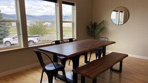 A dining area with a wooden table and chairs, a bench, a potted plant, and a round mirror on the wall.