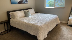 A bedroom with a bed, a nightstand, a window, and a painting on the wall.