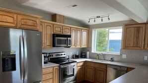 A modern kitchen with stainless steel appliances, wooden cabinets, granite countertops, and a window providing natural light.