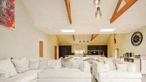 Ein geräumiges Wohnzimmer mit einem großen, weißen Ecksofa, einer Küche im Hintergrund und einem modernen Kronleuchter.