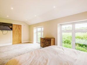 A bedroom with a large bed, a wooden dresser, and a wardrobe. There are two windows providing a view of greenery outside. - The Gallery Barn - UK39368 (Swafield)