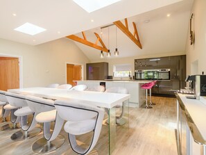 A modern kitchen with stainless steel appliances, a dining area with white chairs, and a wooden ceiling structure. - The Gallery Barn - UK39368 (Swafield)