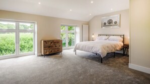 Ein Schlafzimmer mit einem großen Bett, einer hölzernen Kommode und einem Fenster mit Blick auf Grünflächen.