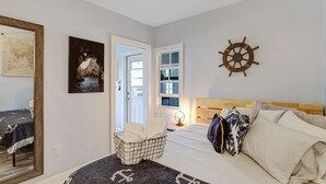 Un dormitorio con cabecera de madera, decoración con timón de barco, cama con almohadas, mesita de noche con lámpara y ventana con vistas.