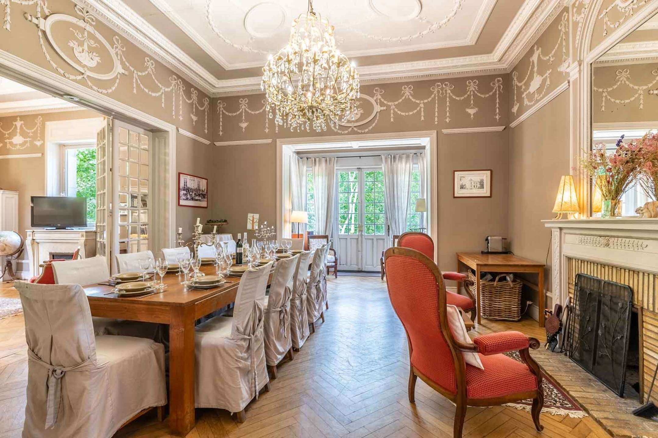 A dining room with a long table set for a meal, a chandelier, and a fireplace.