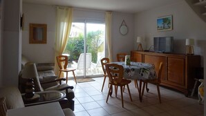 Zona pranzo con tavolo e sedie, televisore su un mobile e una porta scorrevole in vetro che dà su un giardino.