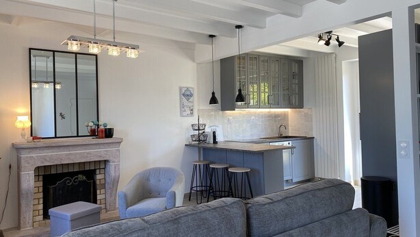 Een moderne woonkamer met een open haard, grijze banken en een keuken met barstoelen.