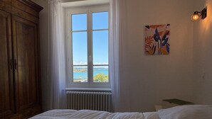 Een slaapkamer met een groot raam, een radiator, een houten garderobe en een schilderij aan de muur.