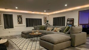 A modern living room with a sectional sofa, a coffee table, and a patterned rug. - The Winsor Lodge | Saco River Group Retreat with Bar, Arcade, Hot Tub & Sauna (Conway)