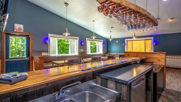 A modern kitchen with a central island, stainless steel sinks, and pendant lighting. - The Winsor Lodge | Saco River Group Retreat with Bar, Arcade, Hot Tub & Sauna (Conway)