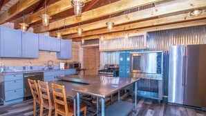 A modern kitchen with wooden beams, a stainless steel island, and a large refrigerator. - The Winsor Lodge | Saco River Group Retreat with Bar, Arcade, Hot Tub & Sauna (Conway)