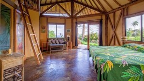 A room with a bed, a sofa, a ladder, and a window with a view of greenery. - Kalani Oceanside Retreat (Pahoa)