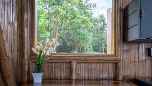 A wooden bench with a potted orchid plant in front of a window overlooking a forest. - Kalani Oceanside Retreat (Pahoa)