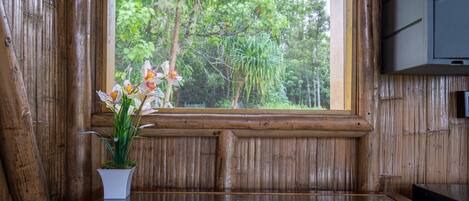 A wooden bench with a potted orchid plant in front of a window overlooking a forest.