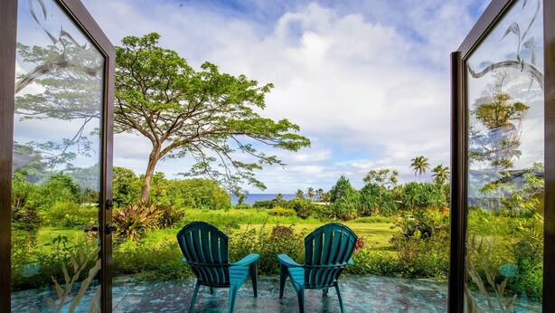 A room with two chairs facing a large window overlooking a lush garden and a tree. - Kalani Oceanside Retreat (Pahoa)