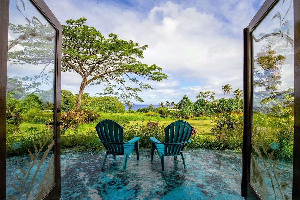 A room with two chairs facing a large window overlooking a lush garden and a tree.