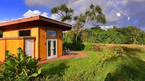 A wooden house with a glass door and windows, surrounded by lush greenery and a visible rainbow. - Kalani Oceanside Retreat (Pahoa)