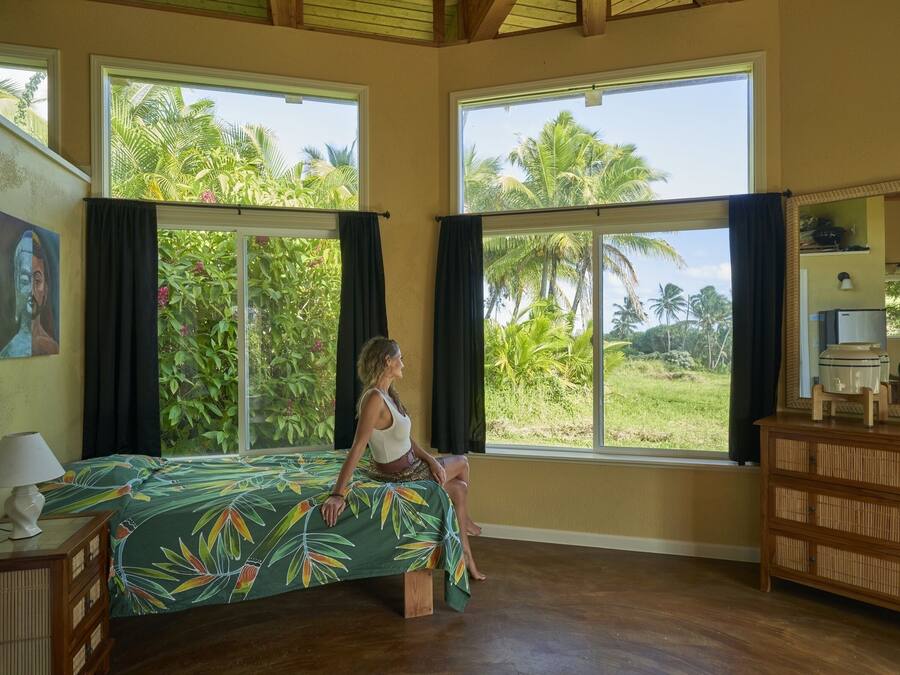 Een kamer met een bed, grote ramen, een houten dressoir en een lamp.