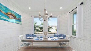 A dining area with a wooden table, white chairs, and a bench. There is a chandelier above the table, and a painting of a sea turtle on the wall. - New Waterfront 3BR townhouse with boat dock and  private heated pool!  (Stuart)