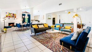 Ein modernes Wohnzimmer mit Kamin, blauen Sofas, einem Essbereich und einer Küche im Hintergrund.