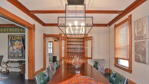 Een ruime eetkamer met een grote houten tafel, groene bekleden stoelen en een kroonluchter.