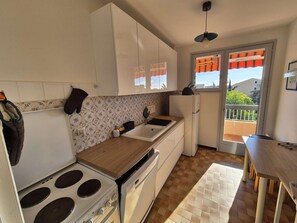 A compact kitchen with a stove, sink, and refrigerator, a wooden countertop, and a view of the outside through a sliding door.