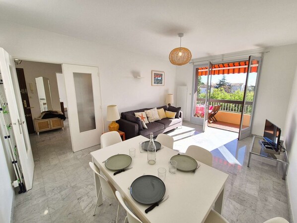 A modern living room with a sofa, dining table, and a balcony with a view.