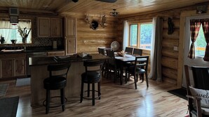 Ein Holzblockhaus-Innenraum mit Küche, Essbereich und Deckenventilator.