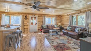 Ein Holzblock-Interieur mit Essbereich, zwei Sofas, einem Couchtisch und einem Deckenventilator.