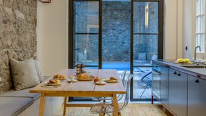 A modern kitchen with a stone wall, a dining table set with food, and a view of a pool through large windows. - Incomparable Plaka's Lux 2bdrm Apt w/Pvt Heated Pool (Athens)