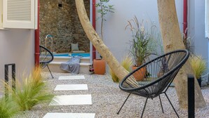 A patio with two black wire chairs, a stone wall, a small pool, and potted plants. - Incomparable Plaka's Lux 2bdrm Apt w/Pvt Heated Pool (Athens)