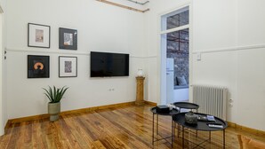 A modern living room with hardwood flooring, a flat-screen TV mounted on the wall, and a small table with a vase and remote control. - Incomparable Plaka's Lux 2bdrm Apt w/Pvt Heated Pool (Athens)