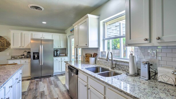 A kitchen with white cabinets, a stainless steel refrigerator, a dishwasher, a granite countertop, and a window. - Merritt Island Oasis w/ Pool ~ 7 Mi to Beach! (Merritt Island)