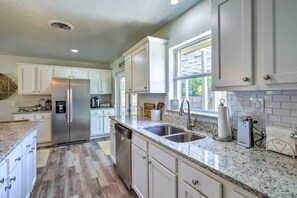 A kitchen with white cabinets, a stainless steel refrigerator, a dishwasher, a granite countertop, and a window. - Merritt Island Oasis w/ Pool ~ 7 Mi to Beach! (Merritt Island)