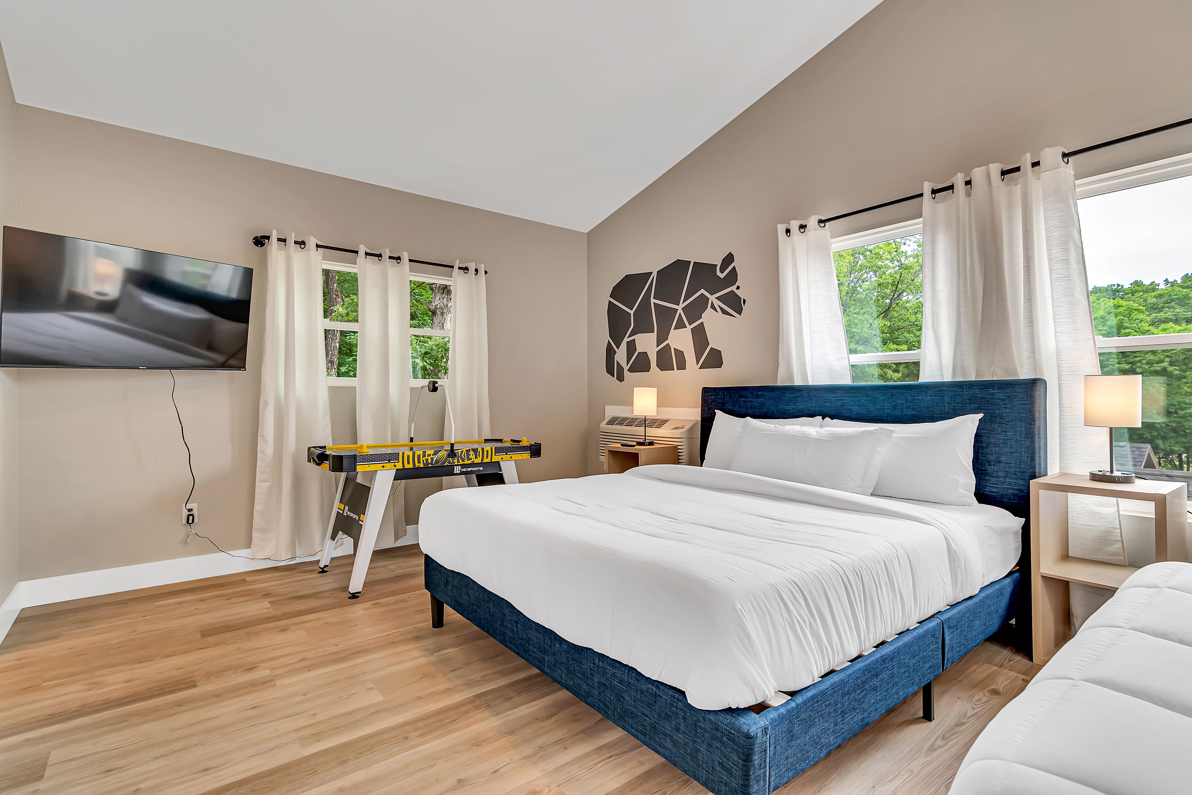 Une chambre moderne avec un grand lit, un téléviseur à écran plat fixé au mur et une fenêtre avec des rideaux.
