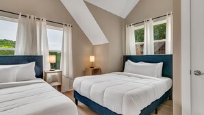 Un dormitorio con dos camas, una mesita de noche, una lámpara y vistas al verde exterior.