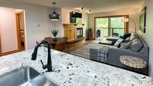 A modern kitchen with a granite countertop, a built-in stove, and a dining area with a wooden table and chairs. - Targhee Creekside Condo - direct shuttle service to Targhee! (Driggs)